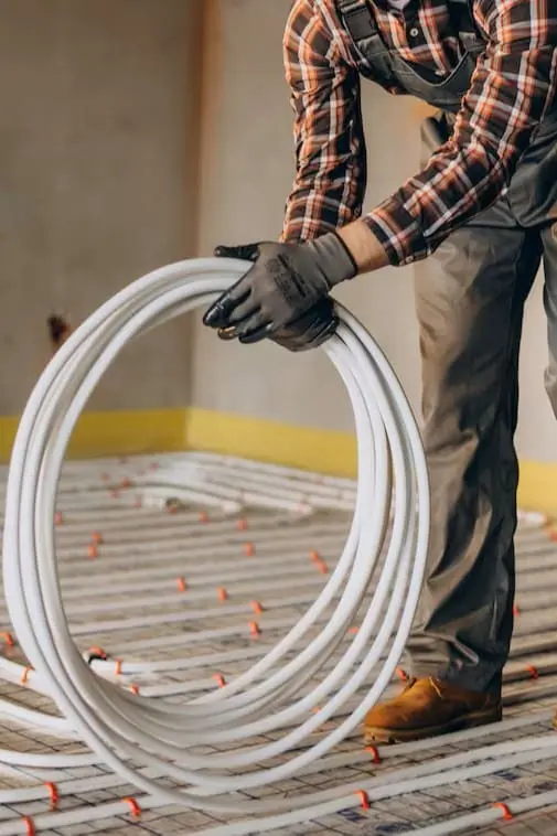 Installateur déroulant des tuyaux pour un plancher chauffant dans une maison